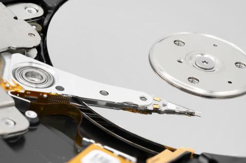 Gros plan sur un disque dur d'ordinateur désassemblé avec la tête magnétique à l'extrémité du bras d'actionnement et le plateau recouvert de matériau magnétique et l'axe du disque.